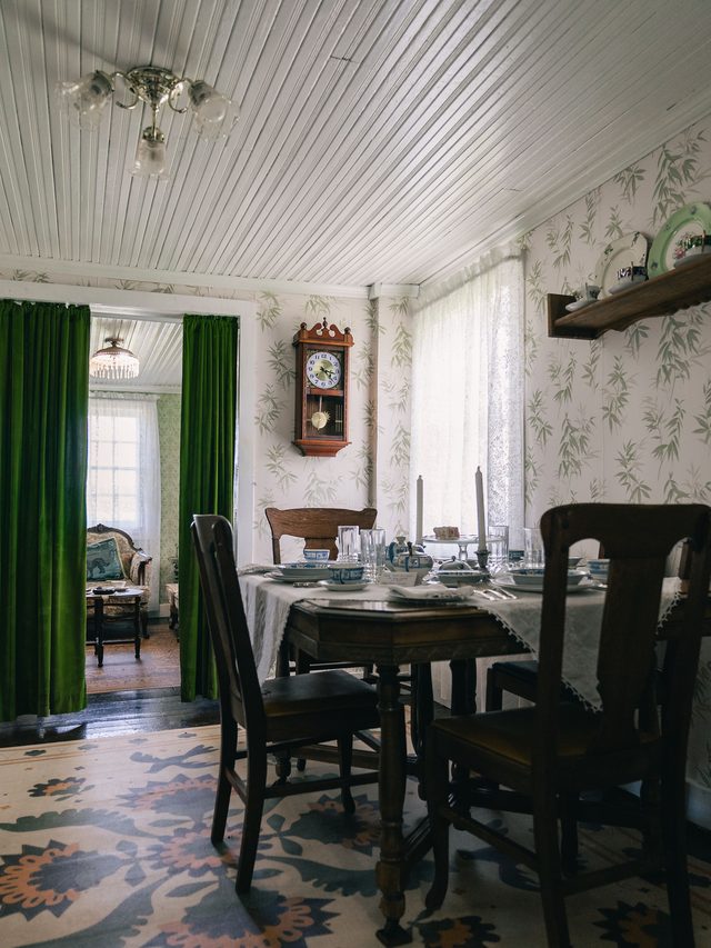 Classic dining room with patterned wallpaper, a dark wood table, and deep green floor-length curtains.