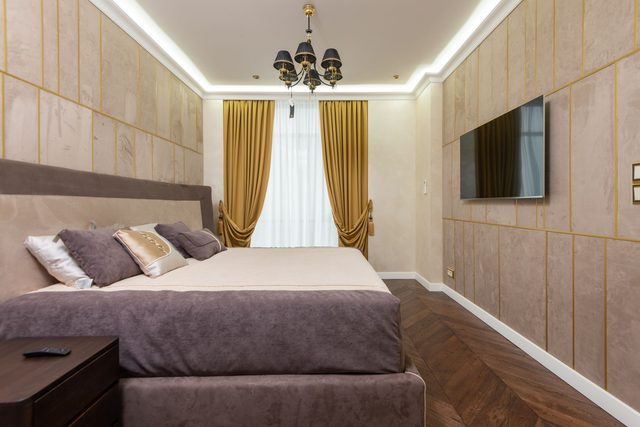 Modern bedroom with beige panelled wallcovering divided by thin gold inlay lines and warm mustard drapes.