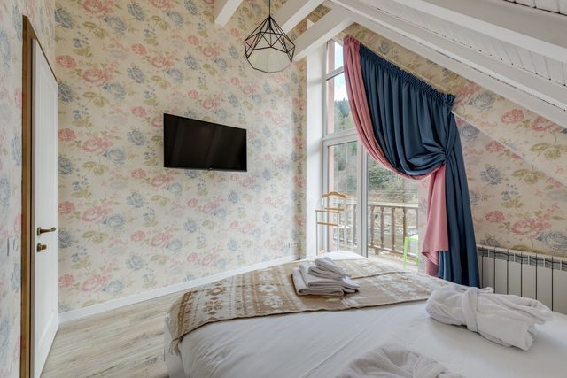 Sloped attic bedroom with soft pink and blue rose floral wallpaper across the walls and a bright balcony window.