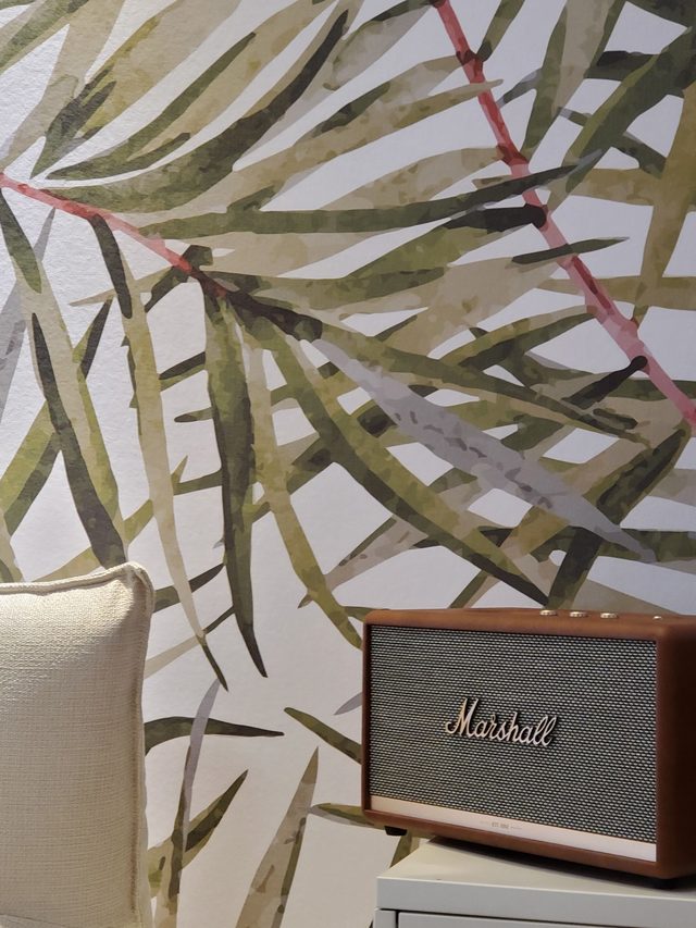 Close view of olive-green watercolour palm-leaf wallpaper on a corner wall above a chest of drawers.
